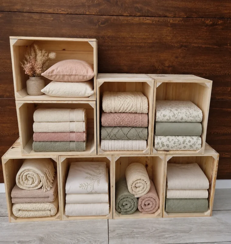 Seven natural pine crates stacked in three tiers, holding folded towels, rolled towels, bedding and cushions
